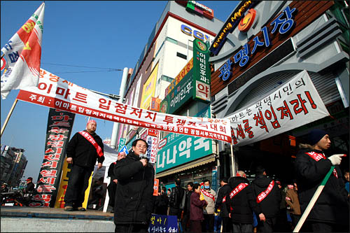 경기도 광명사거리에 들어선 이마트 메트로 광명점이 개점한 24일 오전 광명시장 상인들이 이마트 입점저지를 위한 집회를 열고 있다. 이마트 메트로 광명점은 광명시장 바로 왼쪽 흰 건물 지하에 350평 규모의 매장을 갖추고 있다.
 